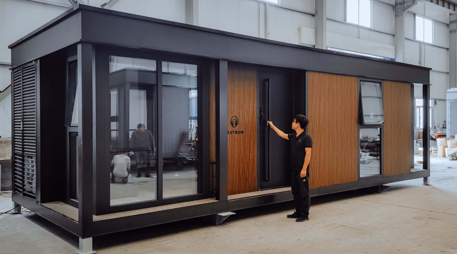 Person standing by a modern modular home in a warehouse.